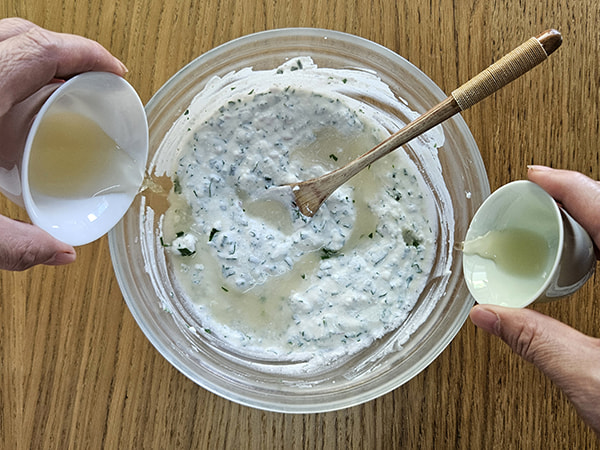 Deux mains versant du vin blanc et du vinaigre de cidre pour assaisonner le fromage blanc aux herbes