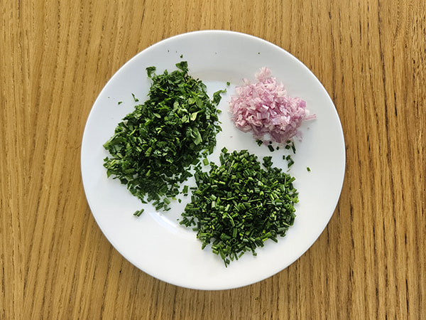 Assiette contenant du persil, de la ciboulette et une échalote finement ciselés