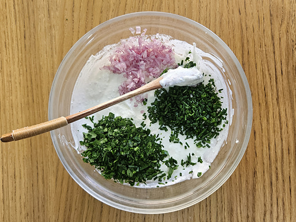 Persil, ciboulette et échalote ciselés déposés sur la base de fromage frais dans un saladier.
